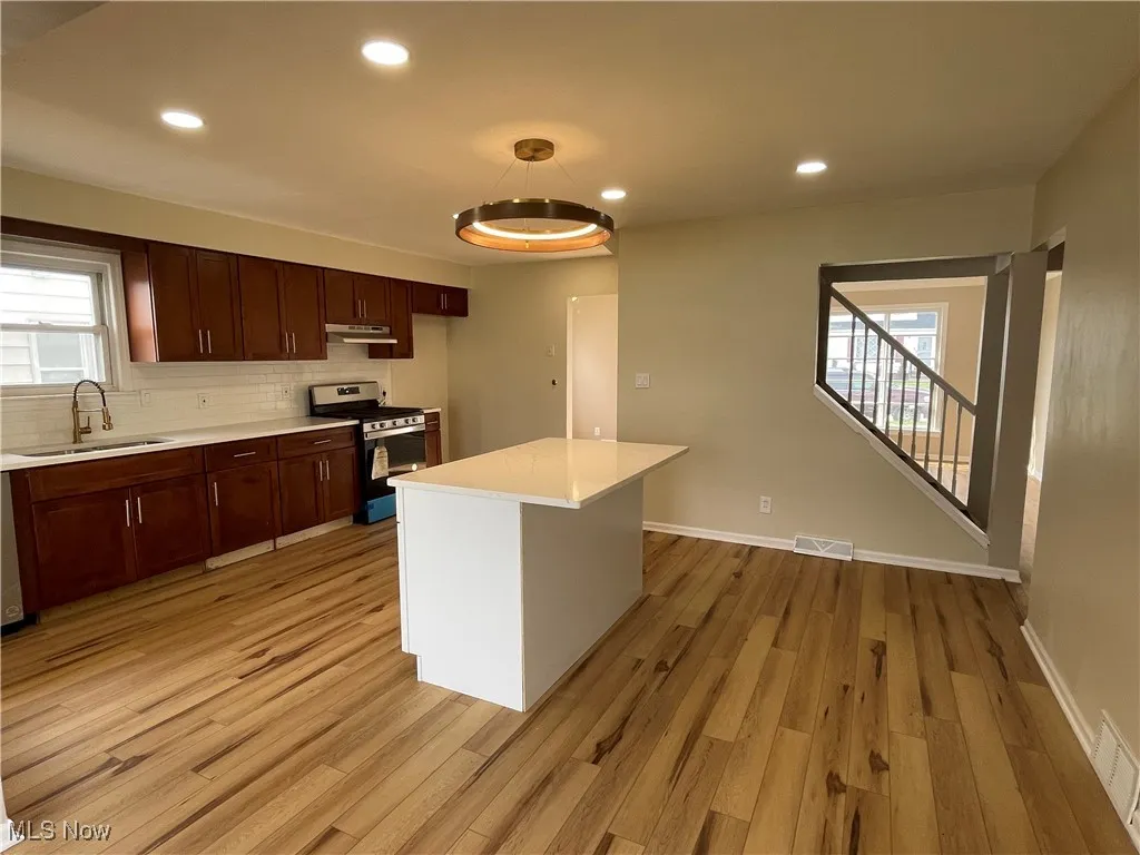 Kitchen with stainless steel stove, light countertops, light wood-type flooring, recessed lighting, and decorative backsplash