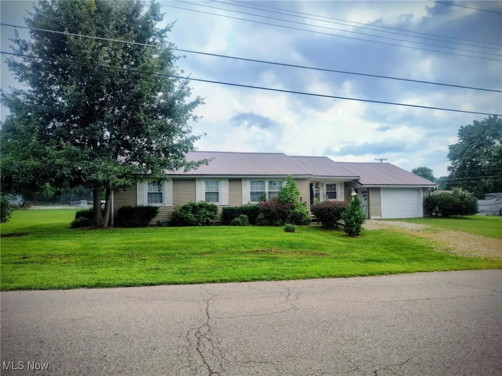 Ranch-style home featuring driveway, an attached garage, a metal roof, and a front lawn