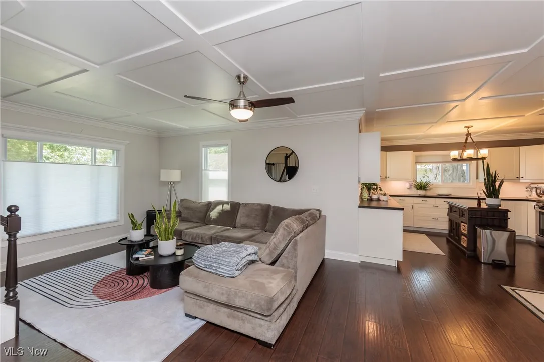 Living area with coffered ceiling, dark wood finished floors, a ceiling fan, ornamental molding, and a chandelier