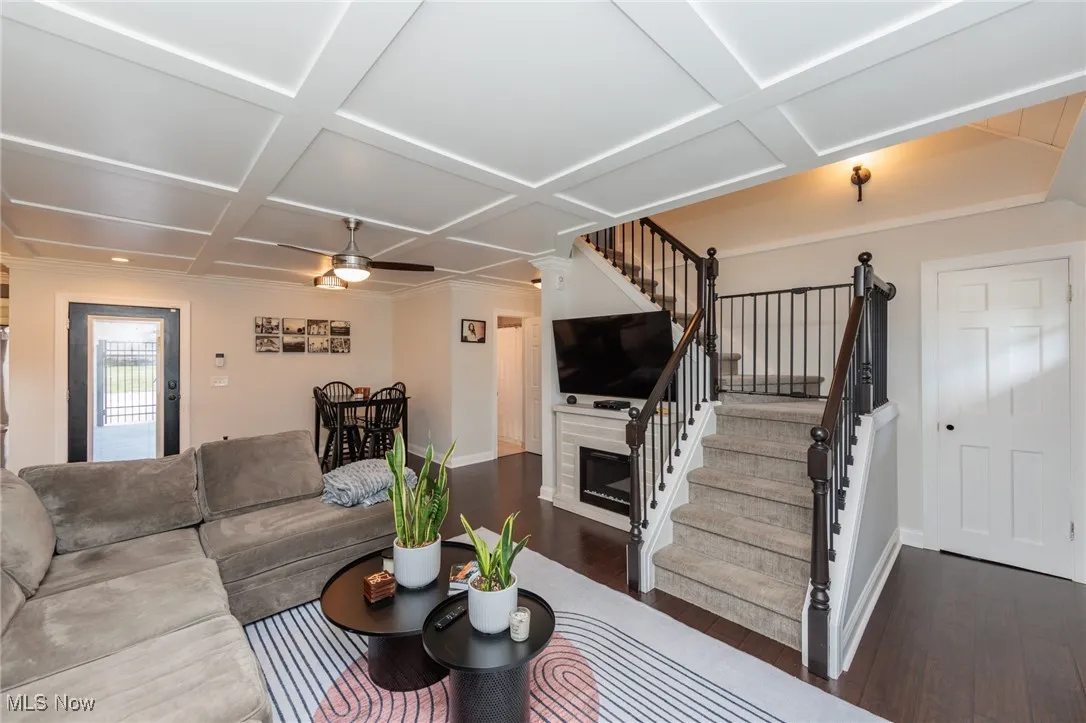 Living room featuring a ceiling fan, stairs, ornamental molding, wood finished floors, and coffered ceiling