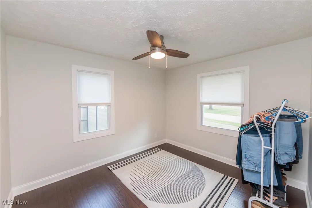 Unfurnished room with dark wood finished floors, healthy amount of natural light, a textured ceiling, and a ceiling fan