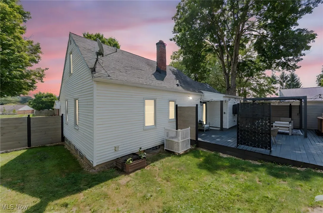 Back of property at dusk with a chimney, a deck, and a shingled roof