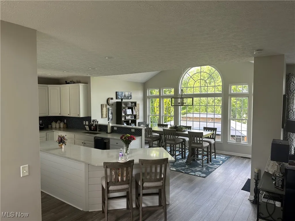 Kitchen featuring a textured ceiling, lofted ceiling, white cabinets, light countertops, and a peninsula