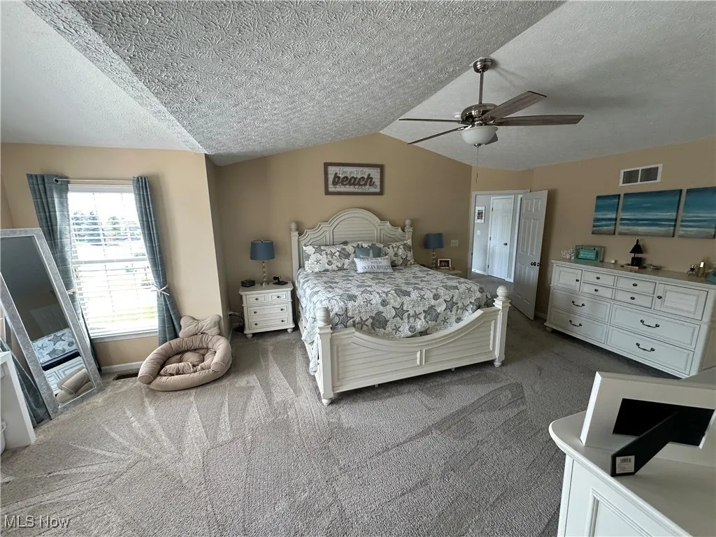 Bedroom with lofted ceiling, dark carpet, a textured ceiling, and ceiling fan