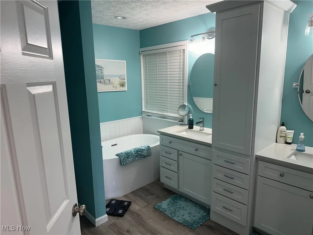 Bathroom with a textured ceiling, vanity, a freestanding tub, and wood finished floors