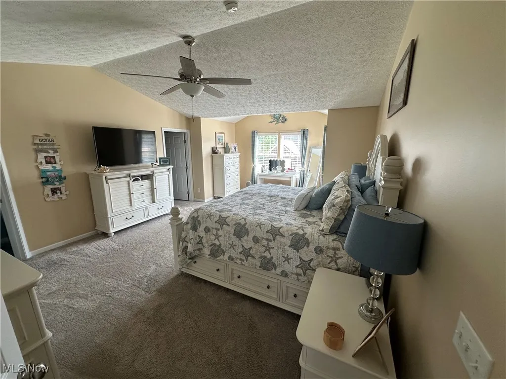 Bedroom with vaulted ceiling, dark carpet, a textured ceiling, and ceiling fan