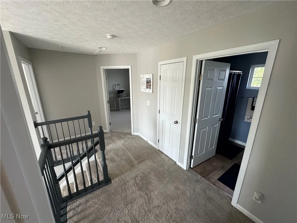 Hallway with an upstairs landing, a textured ceiling, and carpet