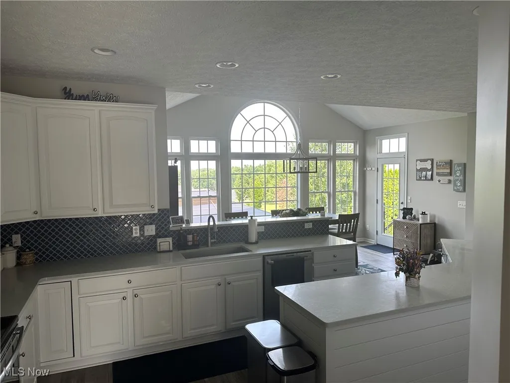 Kitchen with lofted ceiling, a textured ceiling, a peninsula, decorative backsplash, and white cabinets
