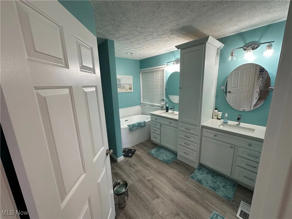 Full bath featuring two vanities, a textured ceiling, a garden tub, and wood finished floors