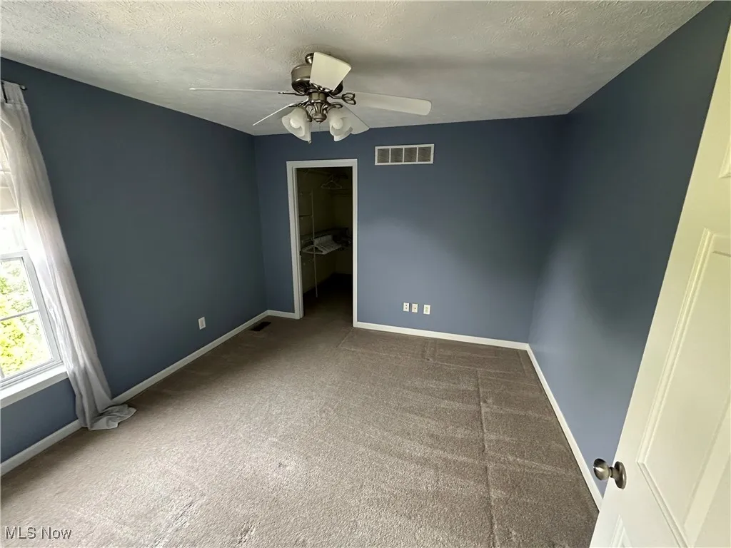 Unfurnished room with a textured ceiling, carpet flooring, and ceiling fan
