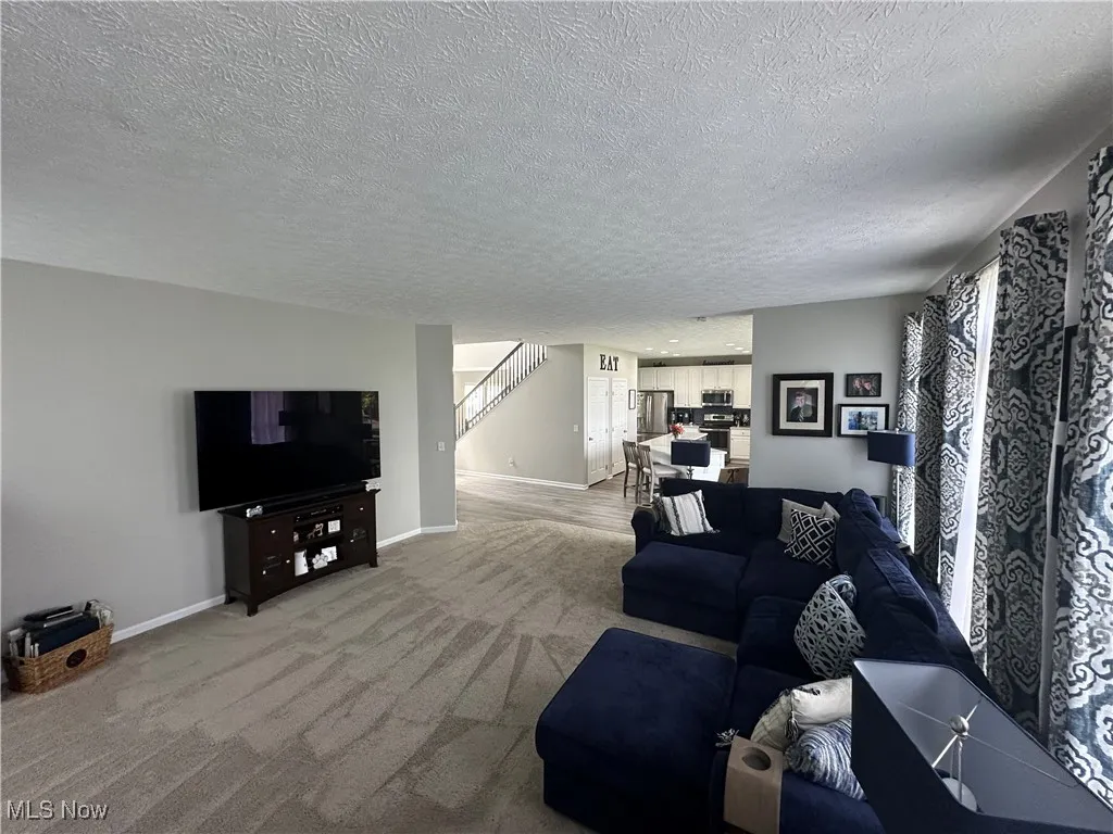 Living room with a textured ceiling, light colored carpet, and stairway