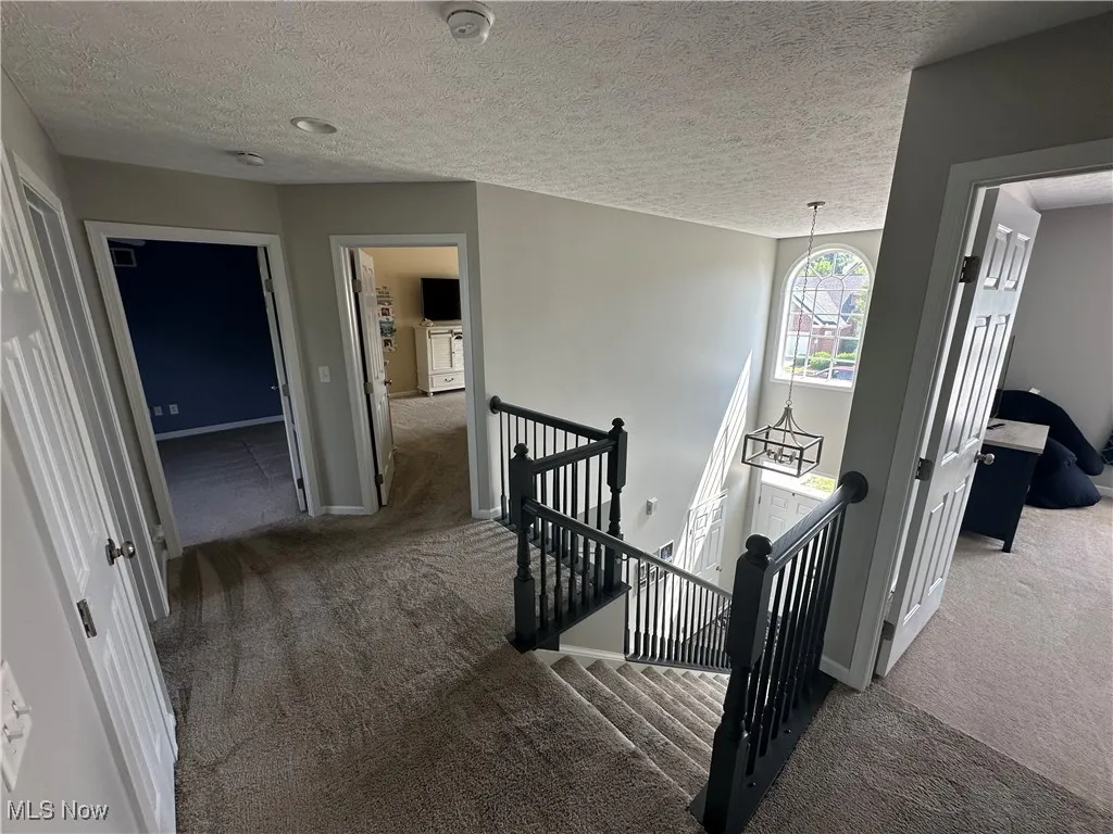 Hall with an upstairs landing, carpet floors, and a textured ceiling