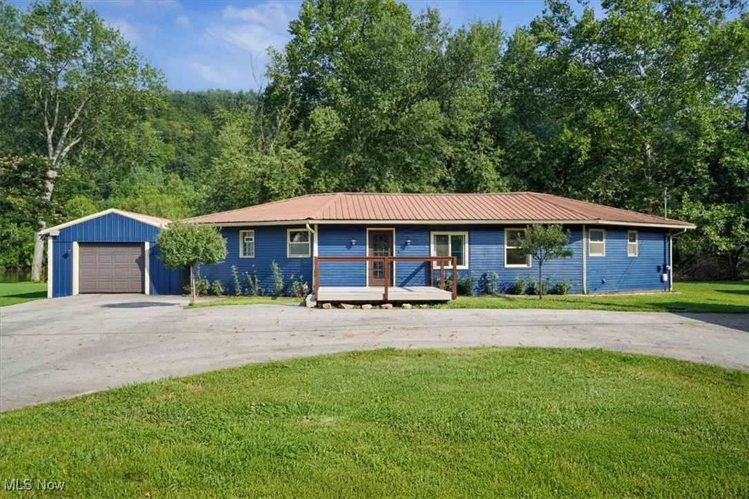 Single story home featuring an outdoor structure, a metal roof, driveway, and a front yard