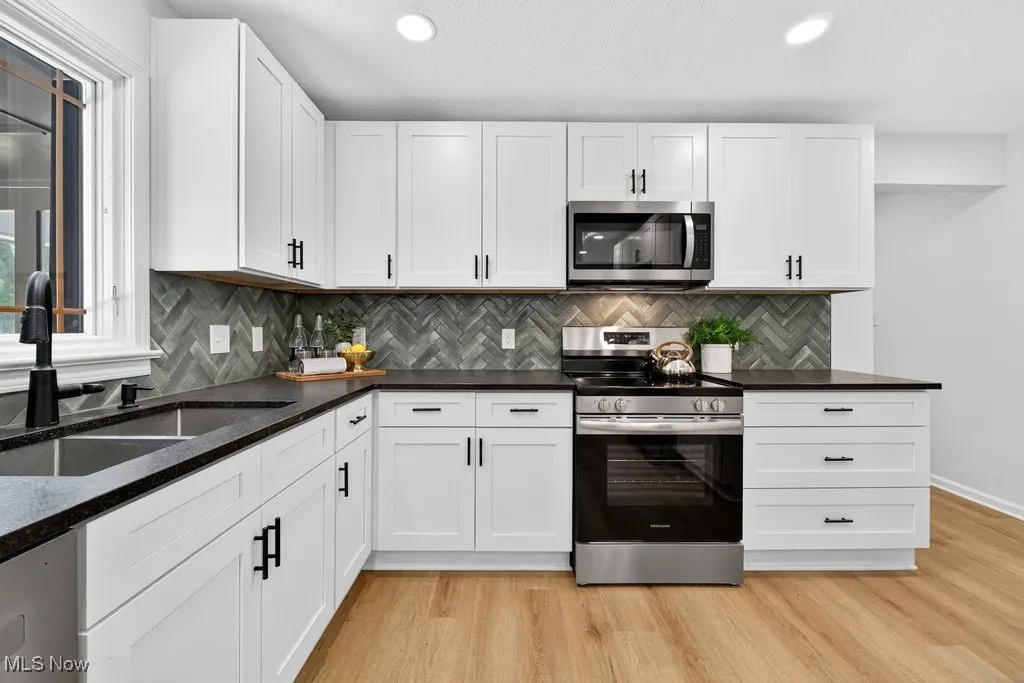 Kitchen featuring stainless steel appliances, light wood finished floors, white cabinets, dark stone counters, and tasteful backsplash