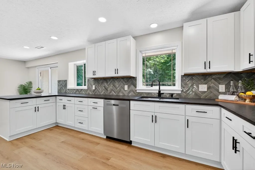 Kitchen featuring a textured ceiling, plenty of natural light, dishwasher, dark countertops, and light wood-style flooring