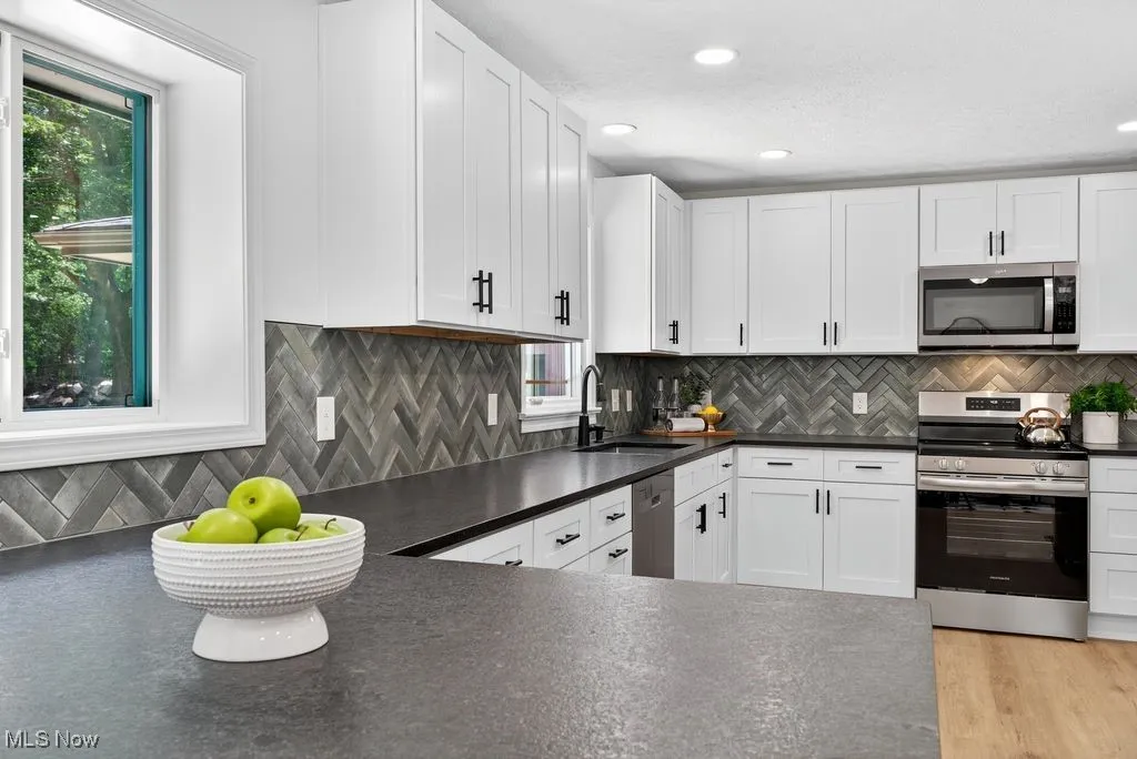 Kitchen featuring dark countertops, appliances with stainless steel finishes, white cabinetry, tasteful backsplash, and recessed lighting