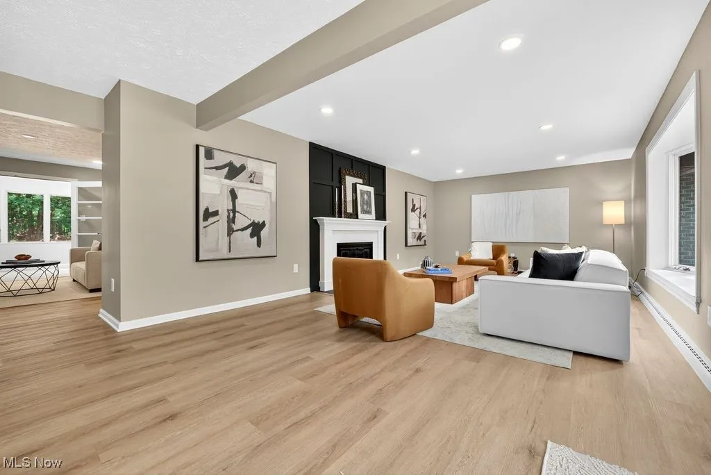 Living area featuring beam ceiling, light wood finished floors, a large fireplace, and recessed lighting