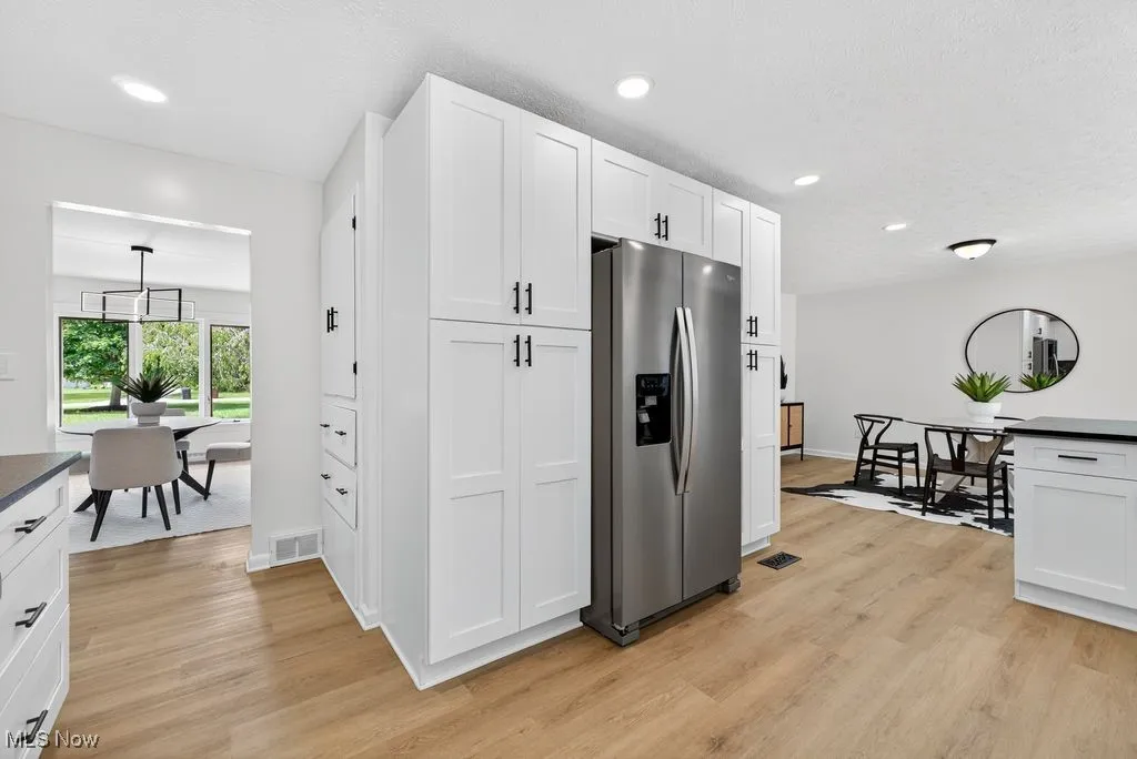 Kitchen with stainless steel refrigerator with ice dispenser, light wood-style flooring, white cabinets, dark countertops, and recessed lighting