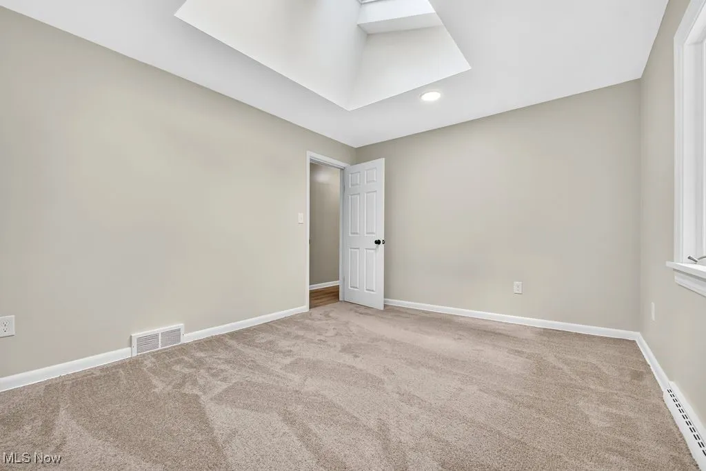 Carpeted empty room with baseboard heating, recessed lighting, and a skylight