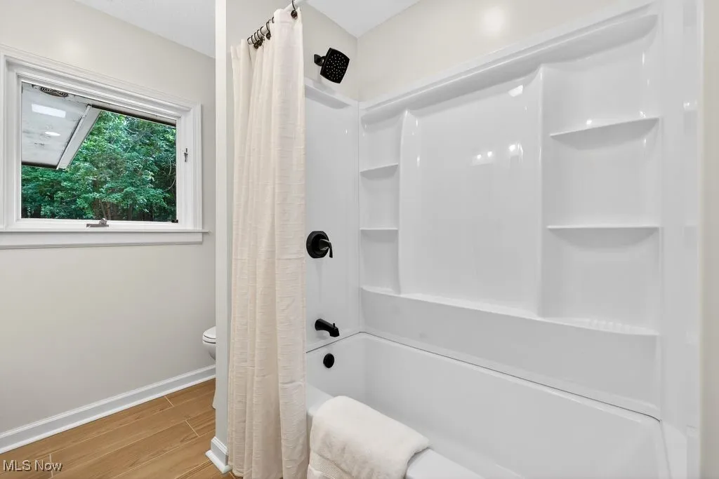 Full bath with wood finished floors and shower / bath combo with shower curtain