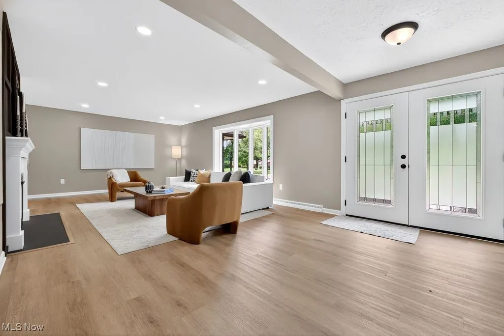 Living area featuring french doors, beamed ceiling, light wood-type flooring, recessed lighting, and a fireplace with flush hearth