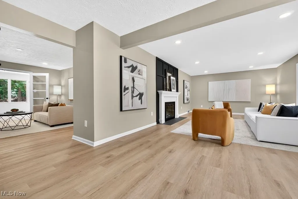 Living area featuring beam ceiling, light wood-style flooring, a fireplace with flush hearth, recessed lighting, and a textured ceiling
