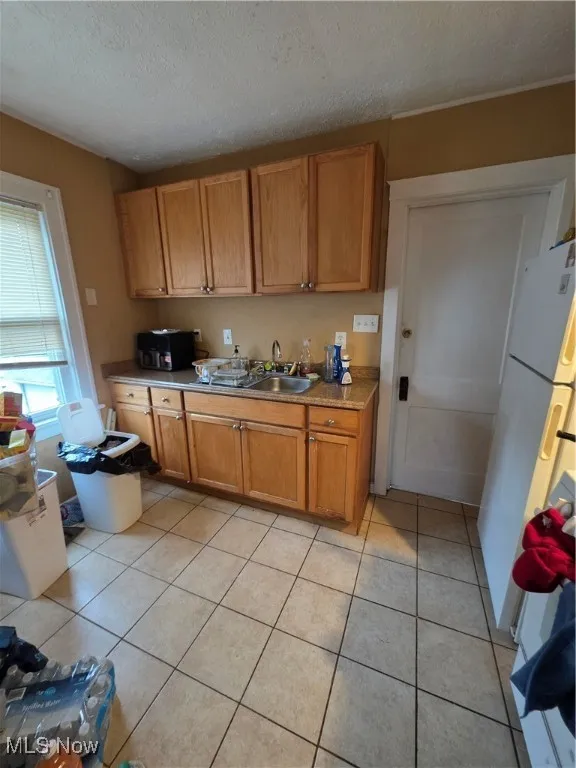 Kitchen with light tile patterned floors, refrigerator, a textured ceiling, and brown cabinetry