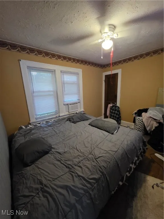 Bedroom with a ceiling fan, a textured ceiling, and cooling unit