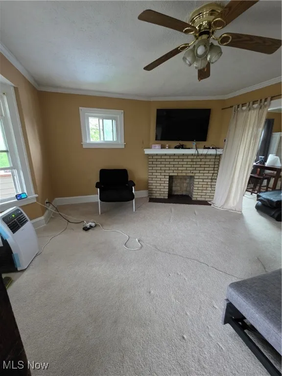 Living area featuring crown molding, ceiling fan, carpet floors, a textured ceiling, and a fireplace