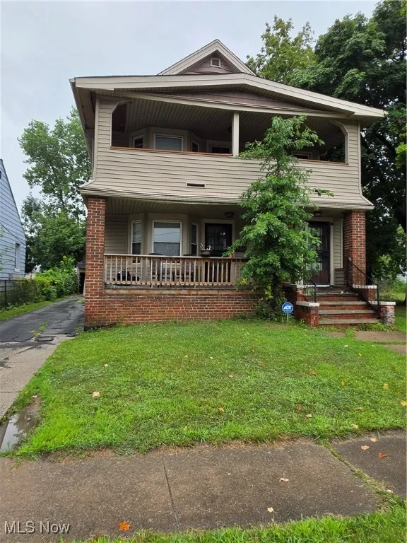 View of front of house with a balcony, covered porch, a front yard, and brick siding