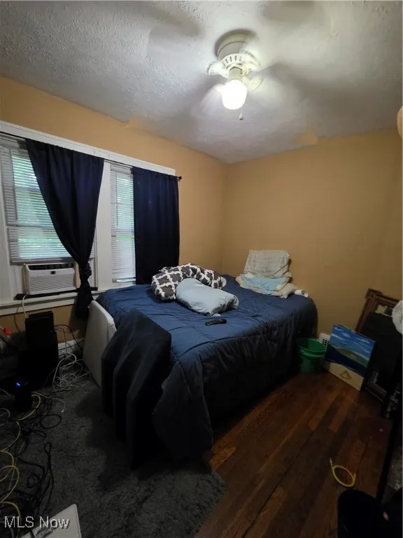 Bedroom featuring a textured ceiling, wood finished floors, a ceiling fan, and cooling unit