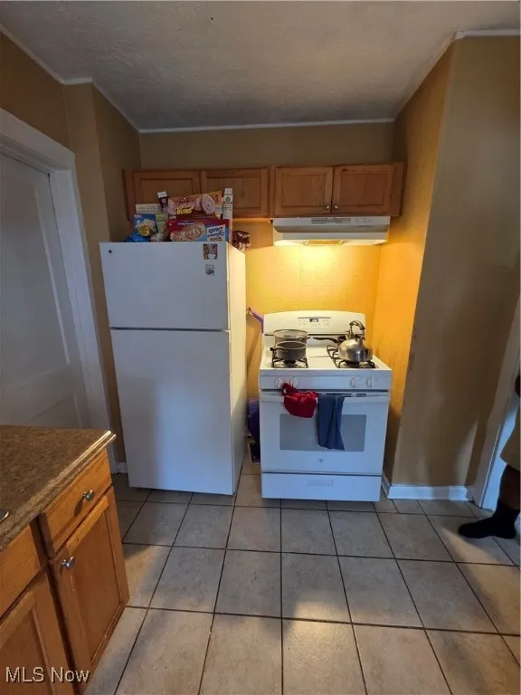 Kitchen featuring fridge, stove, ornamental molding, brown cabinets, and light tile patterned flooring