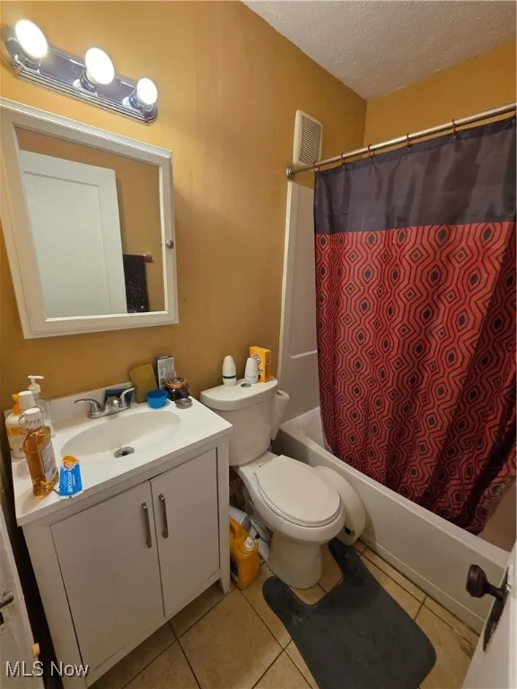 Full bathroom with a textured ceiling, vanity, tile patterned flooring, and shower / bathtub combination with curtain