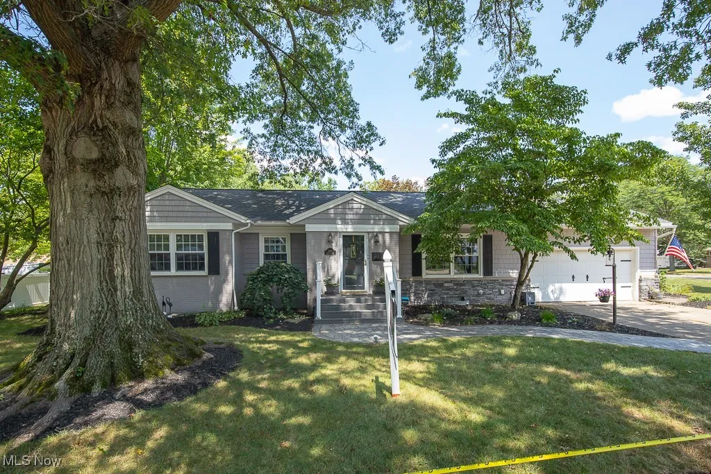 Ranch-style house featuring stone siding, a front yard, an attached garage, and concrete driveway