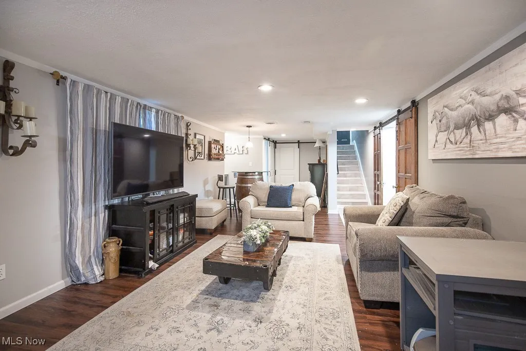 Living area featuring a barn door, stairs, dark wood-style floors, ornamental molding, and recessed lighting