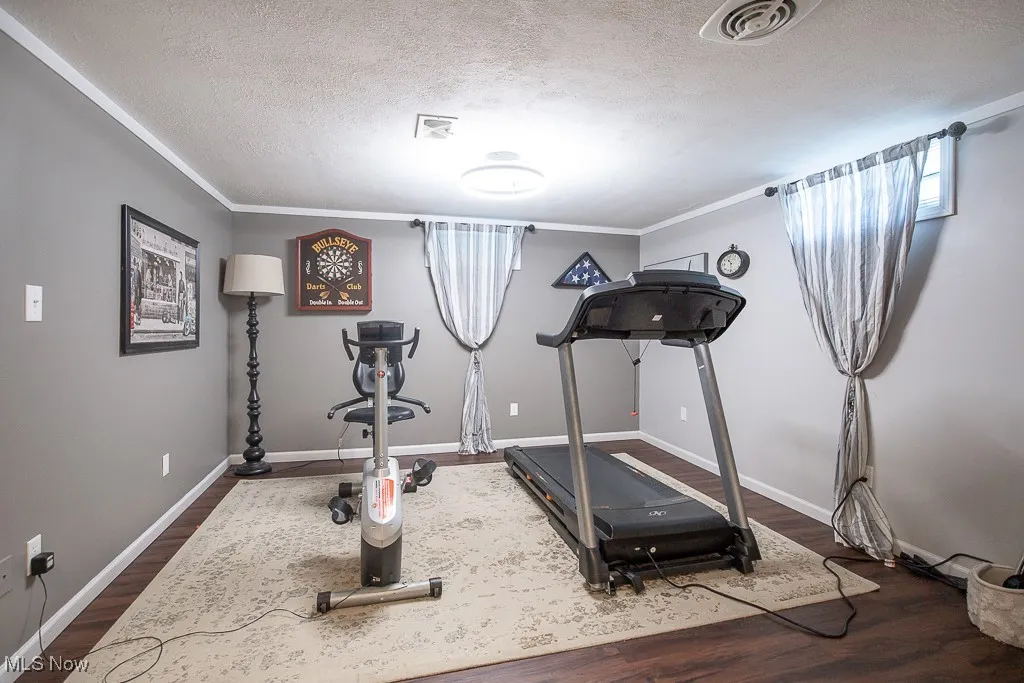 Exercise area featuring dark wood finished floors, a textured ceiling, and ornamental molding