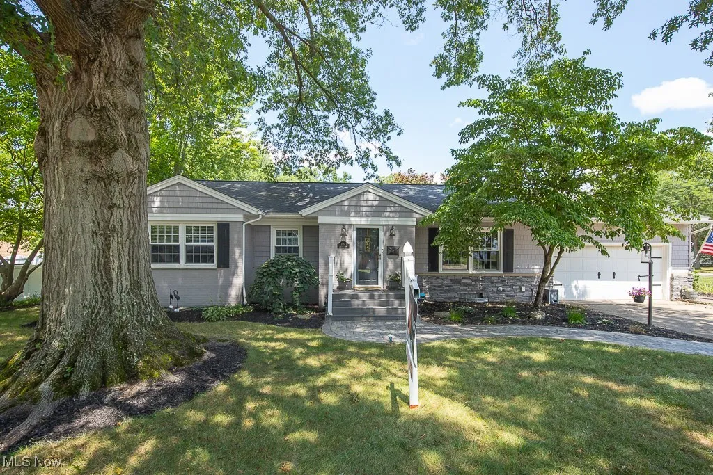 Ranch-style house featuring stone siding, a front lawn, a garage, and driveway