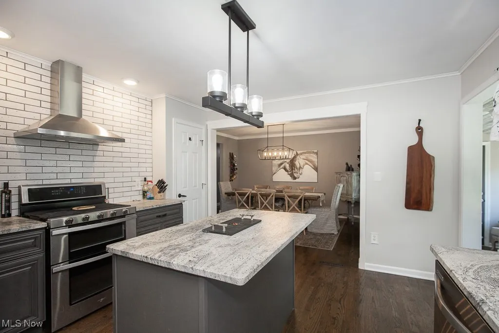 Kitchen with appliances with stainless steel finishes, wall chimney exhaust hood, a center island, ornamental molding, and dark wood finished floors