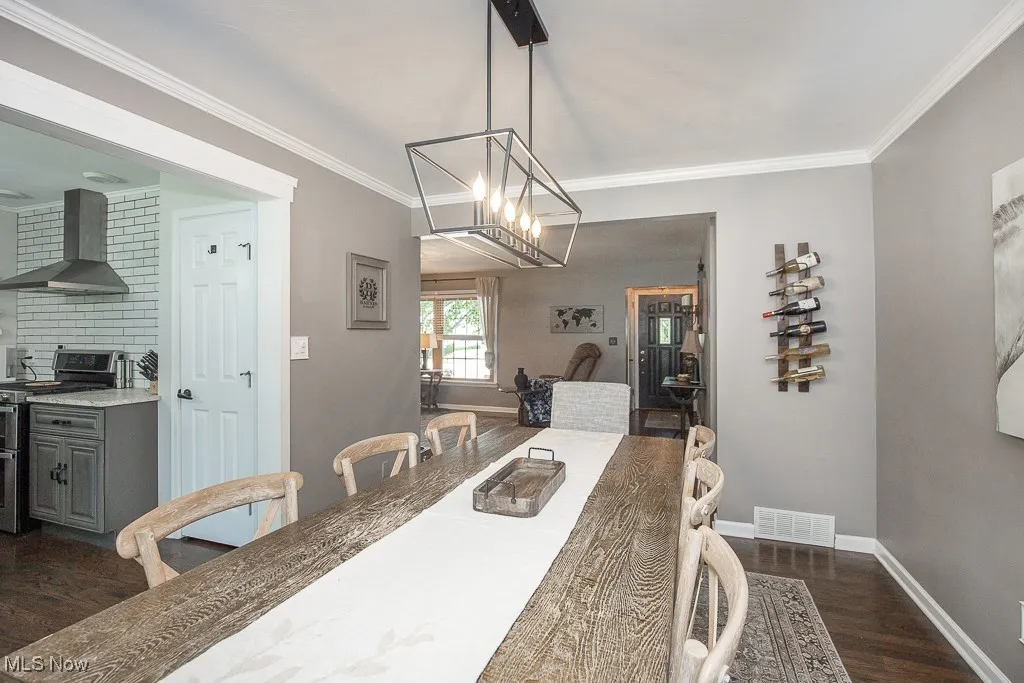 Dining room with dark wood-style flooring, crown molding, and a chandelier