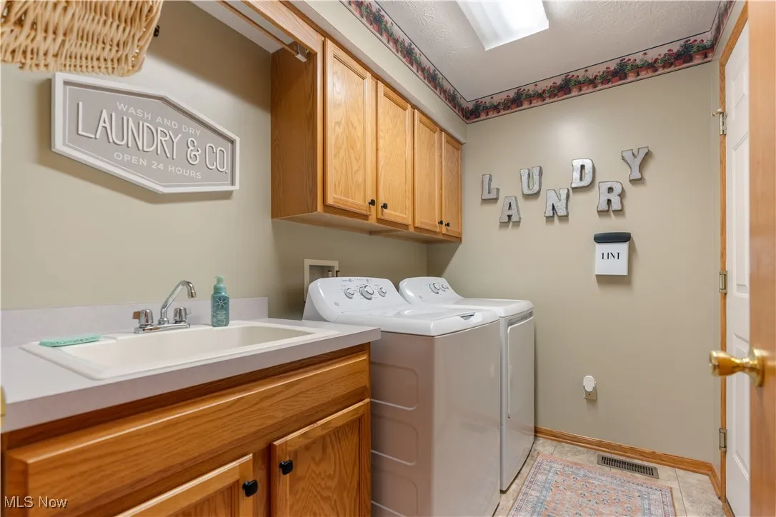 Washroom featuring cabinet space, washing machine and clothes dryer, and light tile patterned floors