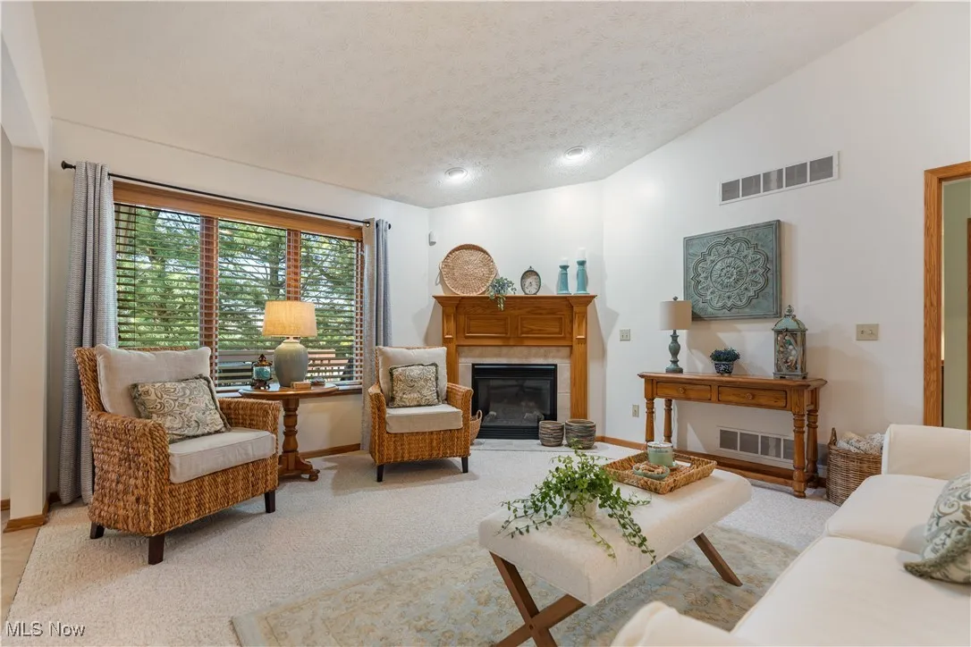 Living area with lofted ceiling, a textured ceiling, a tile fireplace, and light carpet