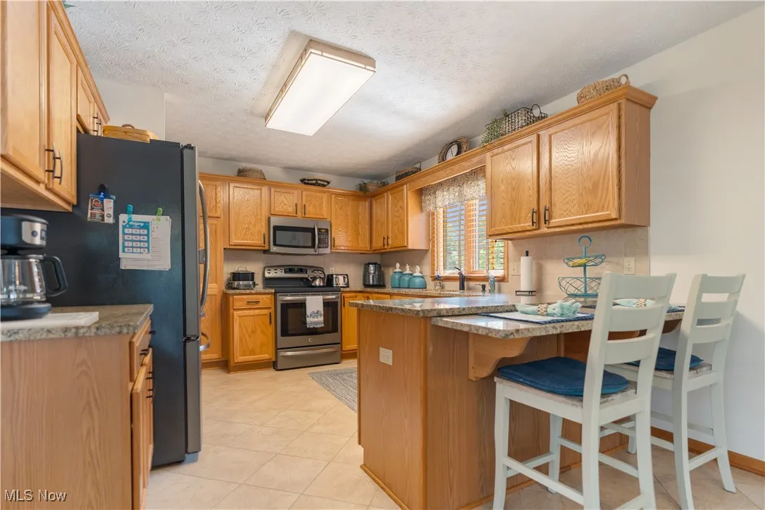 Kitchen featuring a peninsula, appliances with stainless steel finishes, a textured ceiling, a breakfast bar area, and stone countertops