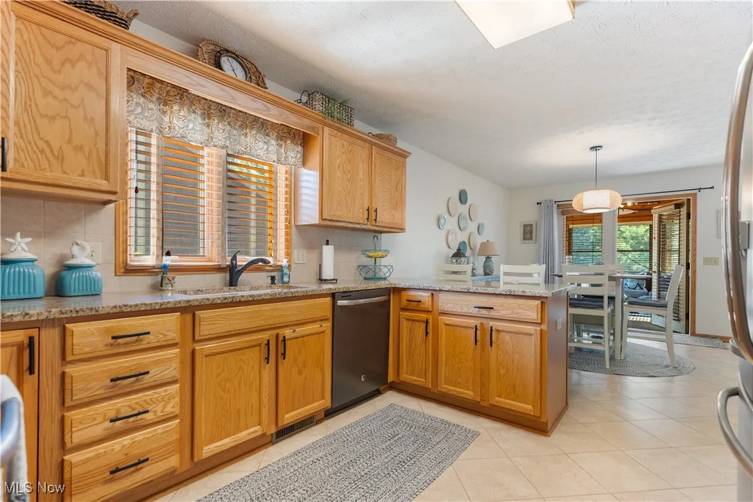 Kitchen with a peninsula, backsplash, dishwasher, light tile patterned floors, and a textured ceiling