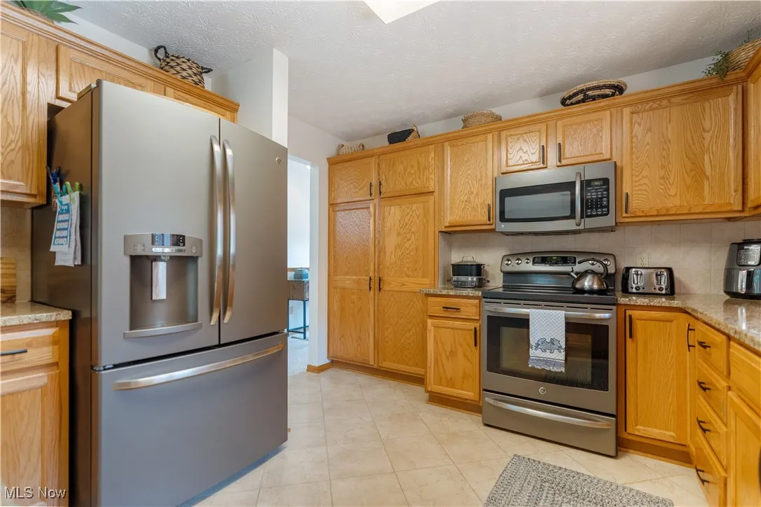 Kitchen featuring appliances with stainless steel finishes, a textured ceiling, decorative backsplash, light stone counters, and light tile patterned floors