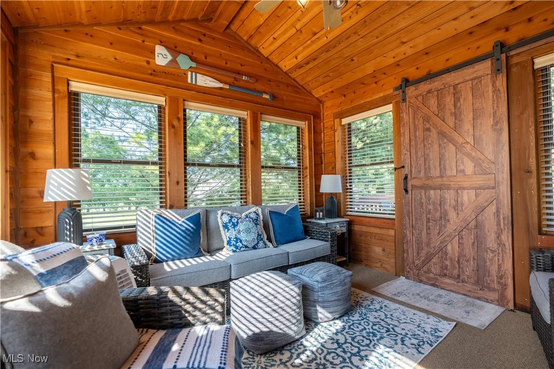 Carpeted living area with vaulted ceiling, a barn door, wood walls, wooden ceiling, and ceiling fan