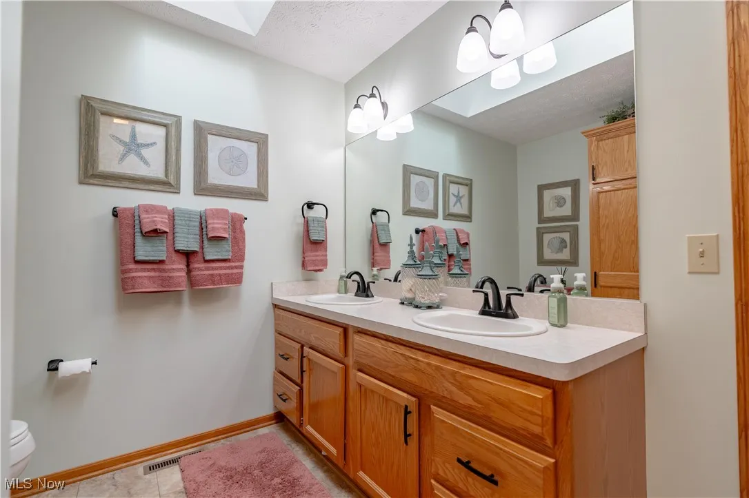 Full bathroom featuring double vanity, a skylight, a textured ceiling, and tile patterned floors