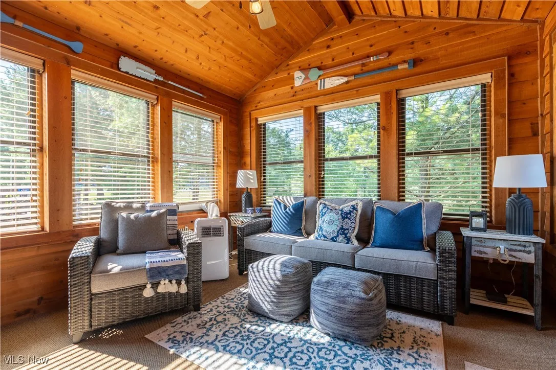 Living room featuring wood walls, vaulted ceiling, wooden ceiling, carpet flooring, and ceiling fan