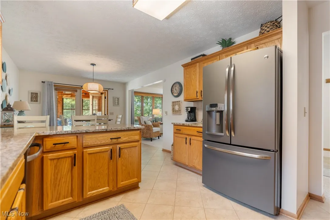 Kitchen with stainless steel appliances, brown cabinets, a textured ceiling, light tile patterned flooring, and pendant lighting