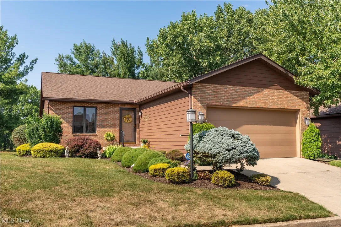 Ranch-style home featuring an attached garage, concrete driveway, a front lawn, brick siding, and a shingled roof