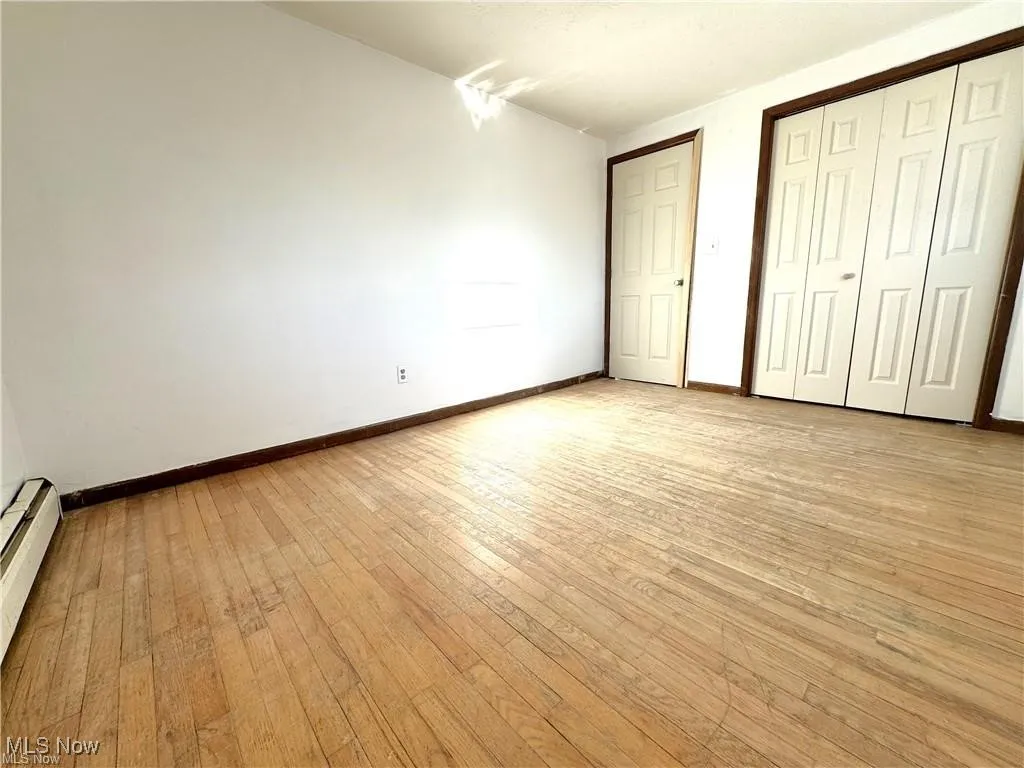 Unfurnished bedroom featuring light wood-type flooring and a baseboard radiator